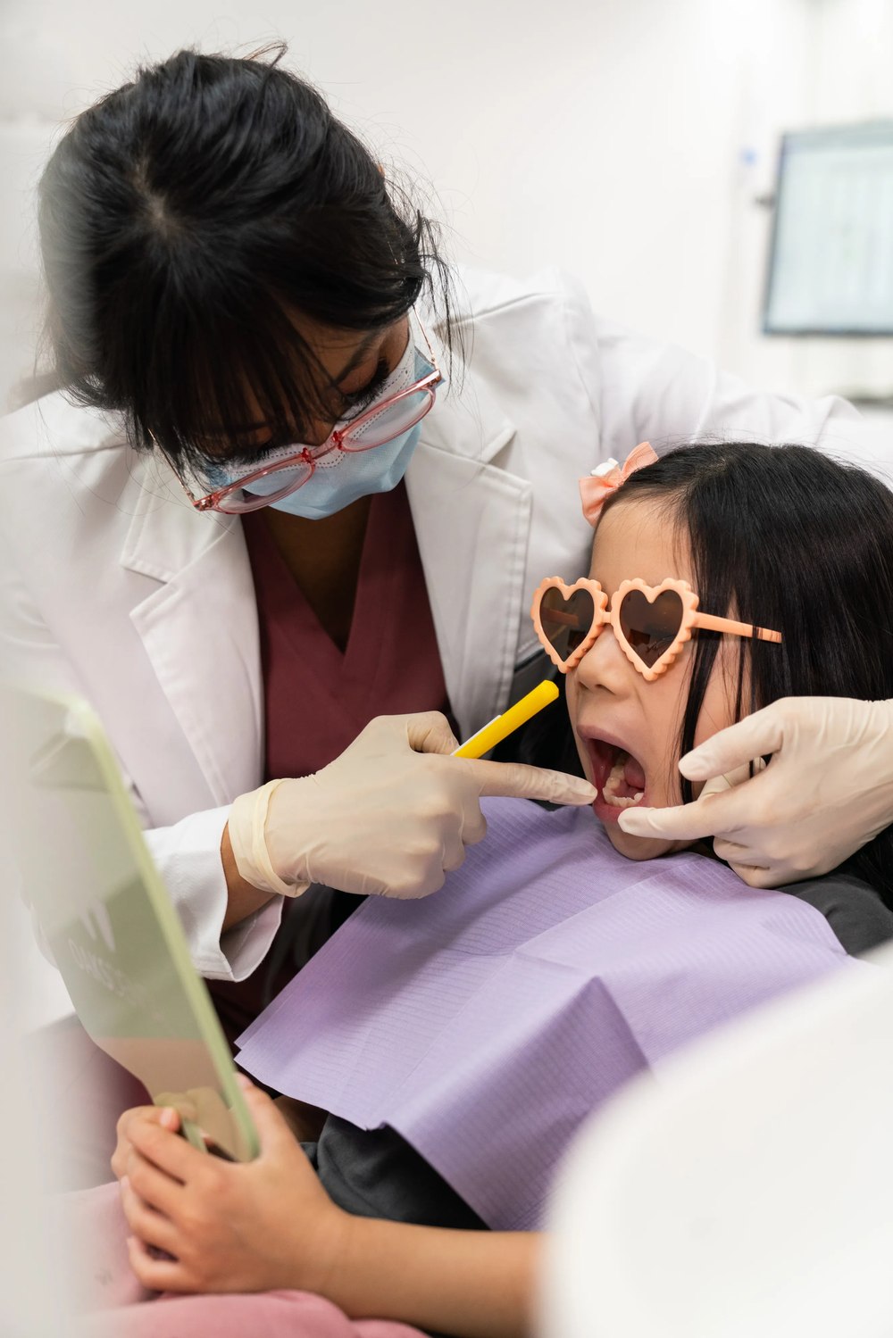 A dentist at Oaks Dental checking a child's bite and the muscles around the mouth while the child holds a mirror