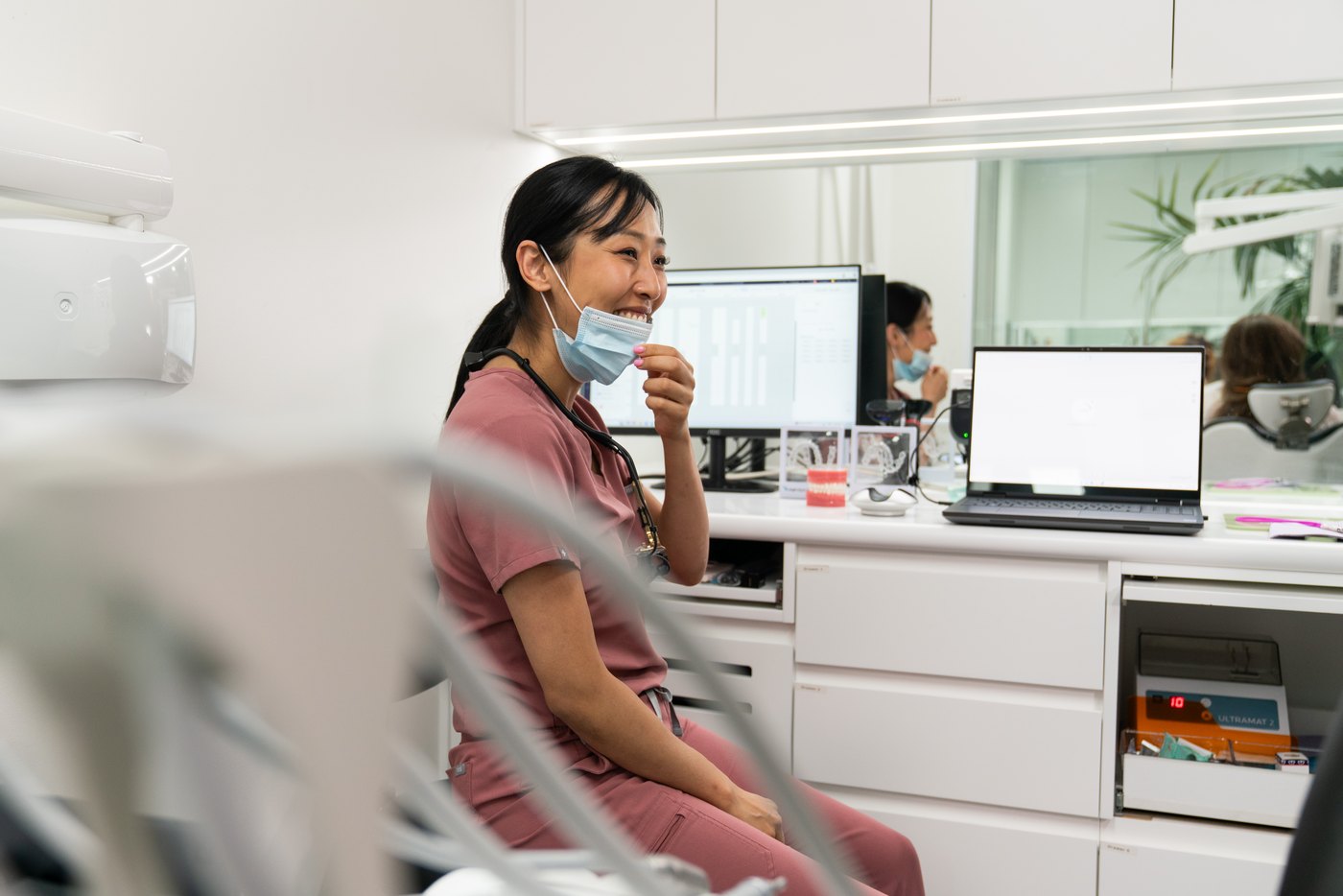 A dentist at Oaks Dental sitting beside the chair in the surgery, talking with a patient, with digital scans and clinical records on the screen behind her