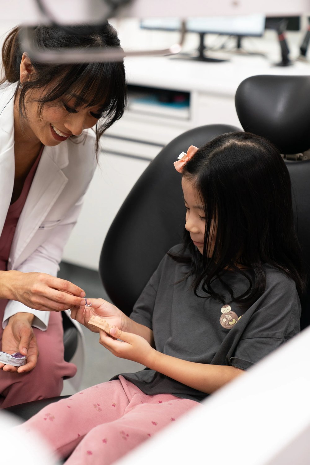 A dentist at Oaks Dental showing a young girl a removable upper appliance and a model of her teeth during an assessment