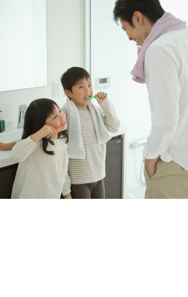 Two young children brushing their teeth with a parent