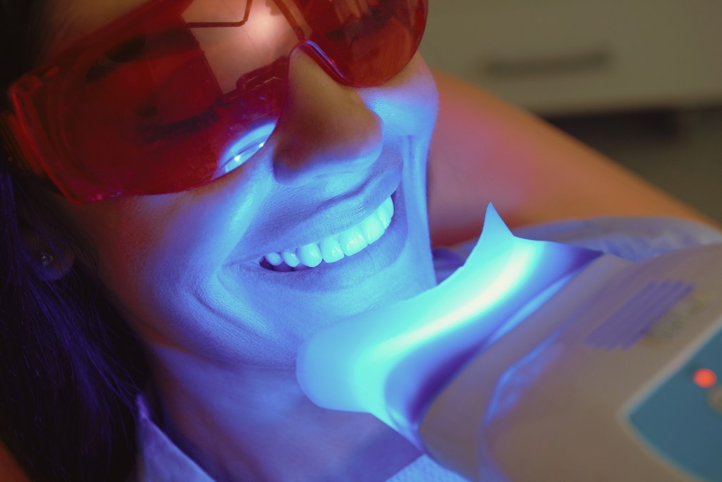 A patient wearing protective glasses during in-chair teeth whitening, with the whitening light positioned over the teeth